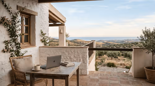 Calm morning terrace scene in Spain with soft natural light and a structured, minimal table vignette (coffee + closed laptop)